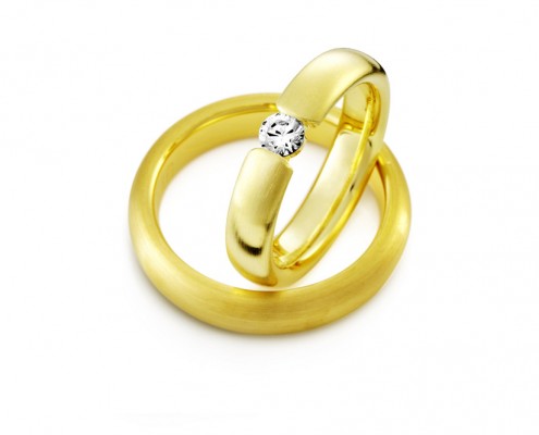 Vielsesringe i guld med et unikt look der har en smuk diamant der bryder ringskinnen midtpå.
