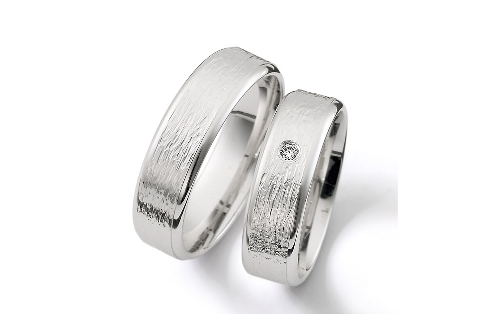 Vielsesringe i børstet og råt look med en enkelt diamant i brilliantslibning i smuk indfatning centralt på ringskinnen.